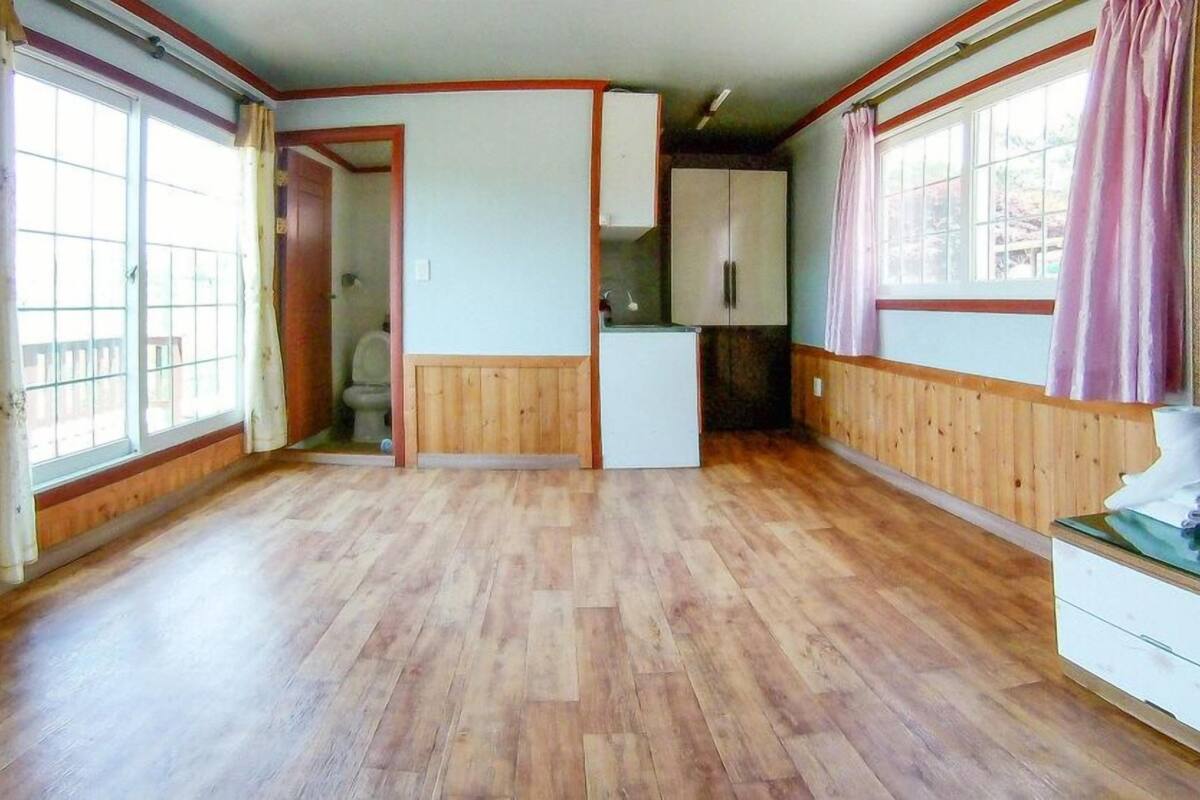 A room with wooden flooring, a white cabinet, and a window with curtains.