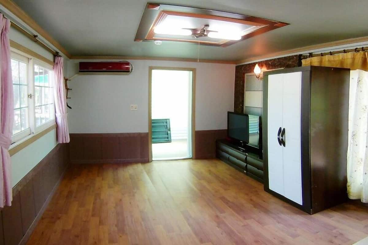 A room with a wooden floor, a television on a stand, a wardrobe, and a ceiling fan.