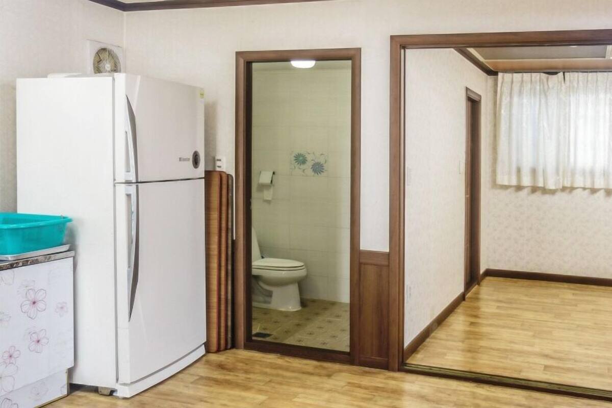 A compact kitchen with a refrigerator, a sink, and a toilet visible through an open door.