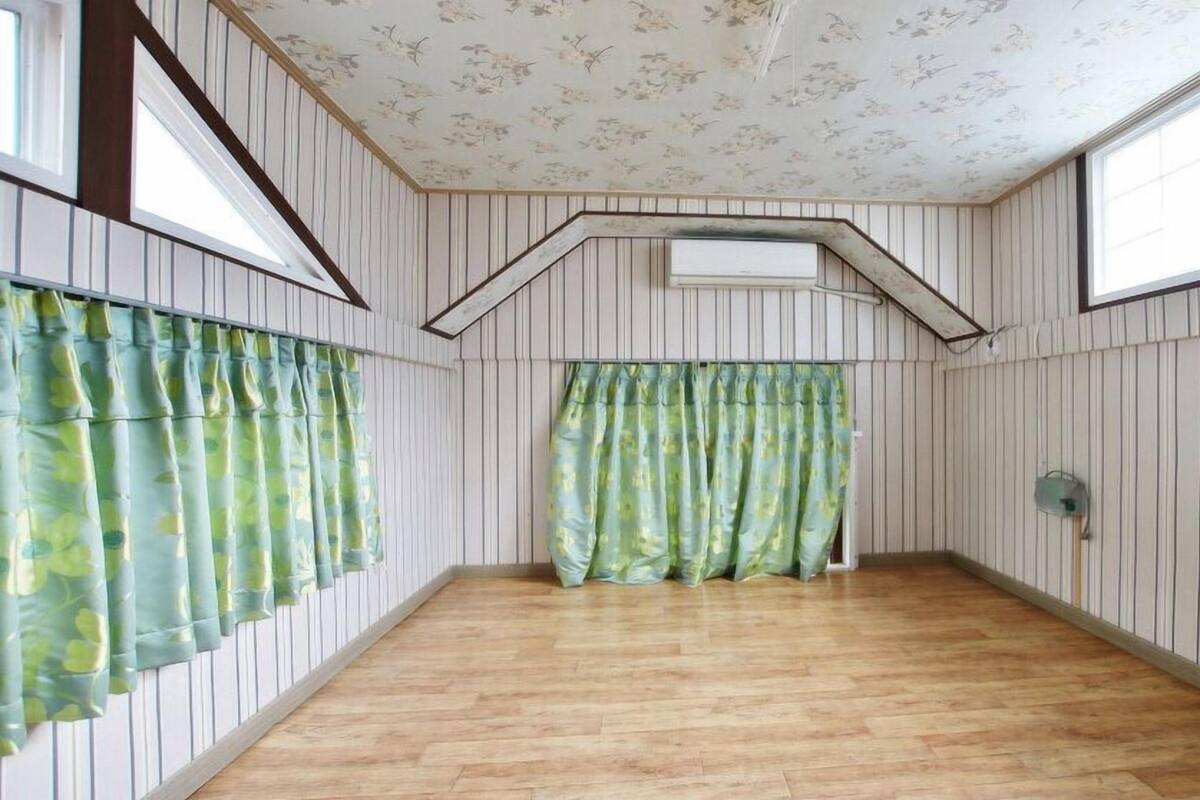 A room with wooden flooring, striped wallpaper, and floral-patterned curtains.