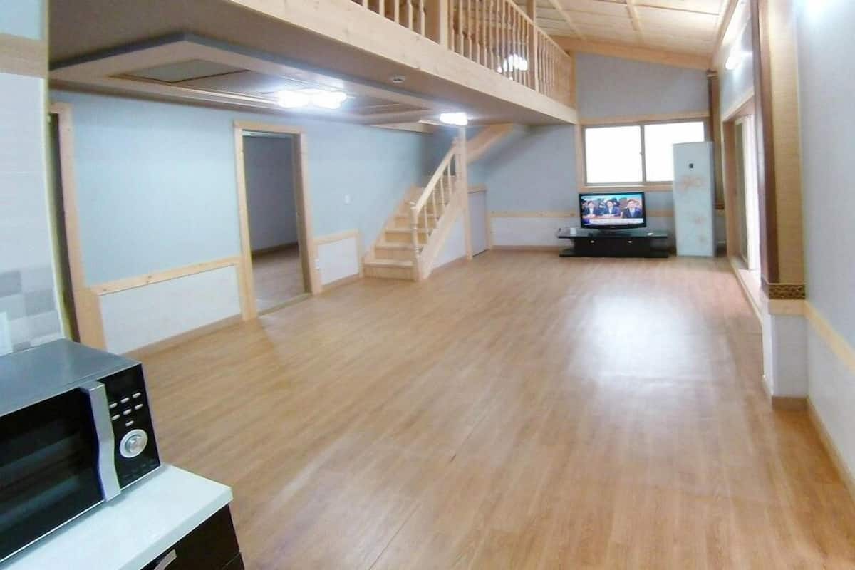 A spacious room with a wooden floor, a staircase, a television, and a microwave.