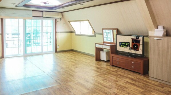 A spacious room with a wooden floor, a desk with a chair, a television, and a cabinet. - Mirim Pension (Incheon)