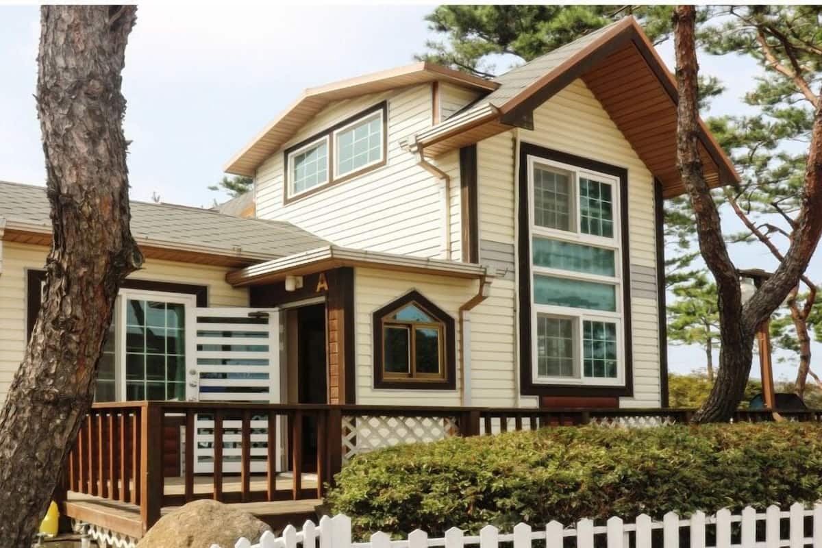 A two-story house with a gabled roof, a front porch with a railing, and a white picket fence.