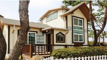 A two-story house with a gabled roof, a front porch with a railing, and a white picket fence.