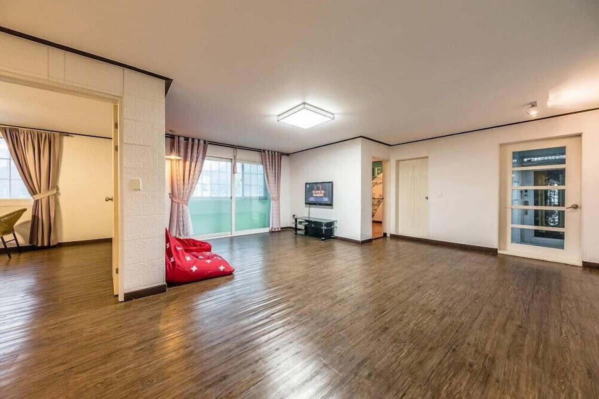 A spacious room with a wooden floor, a red bean bag, a television, and a sliding door.