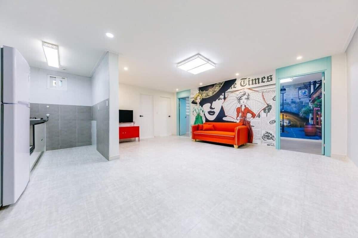 A spacious living area with a red sofa, a mural, and a kitchen area.