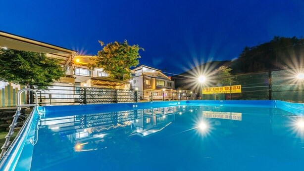 Una piscina con una cerca, un edificio con un letrero y un árbol.
