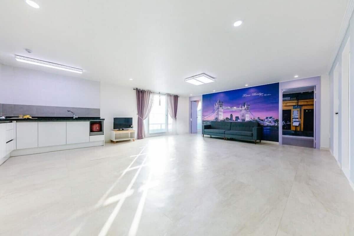 A modern living room with a large window, a sofa, and a kitchen area with cabinets and a countertop.