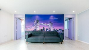 Una habitación con un gran mural en la pared que representa el Tower Bridge, un sofá verde y una puerta que da a otra habitación.