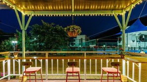 Un espacio de estar al aire libre cubierto, con tres sillas rojas y una maceta colgante de flores.