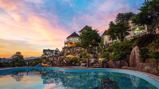 A resort with a swimming pool, a view of the mountains, and a sunset. - Wellbeing log Pension (Gapyeong)