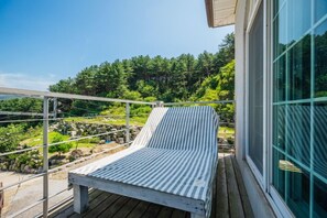 A wooden deck with a striped lounge chair and a glass building with a view of a forested hillside. - Haneul mok Pension (Gapyeong)