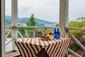 A table with a striped tablecloth, a plate of fruit, and two bottles of water on a balcony with a view of mountains and trees. - Haneul mok Pension (Gapyeong)