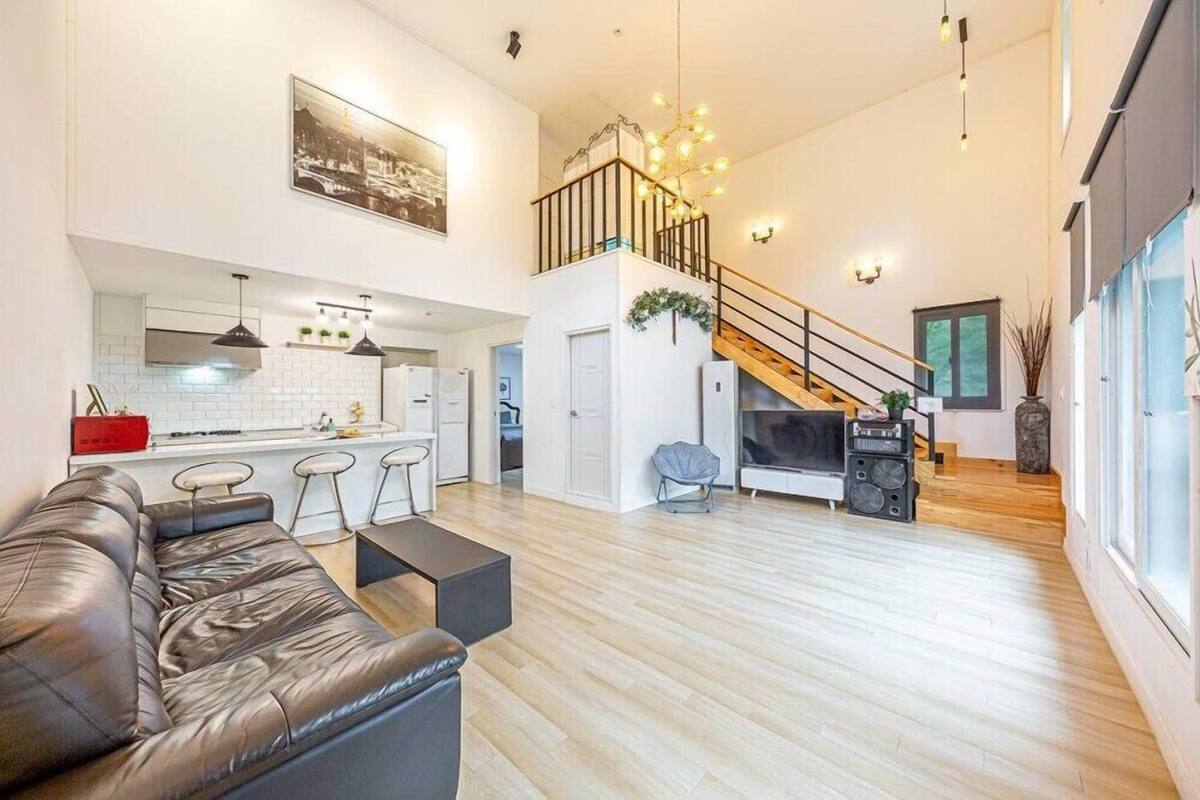 A spacious living area with a leather sofa, a kitchen with a white backsplash, and a staircase leading to an upper level.