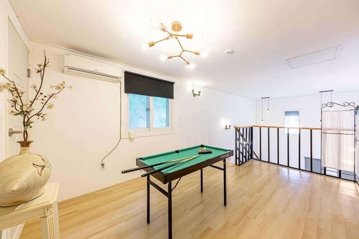 A room with a pool table, a vase with flowers, a ceiling light fixture, and a window with blinds.