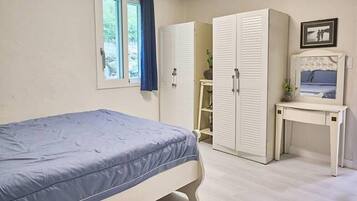 A bedroom with a bed, two wardrobes, a desk with a mirror, and a window with curtains.