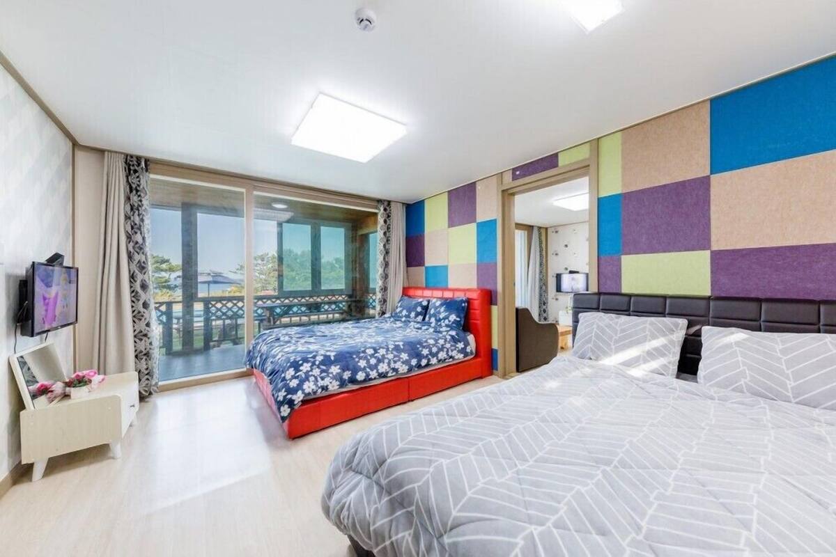 A modern hotel room with a large bed, a smaller bed, a TV, a desk, and a balcony with a view.