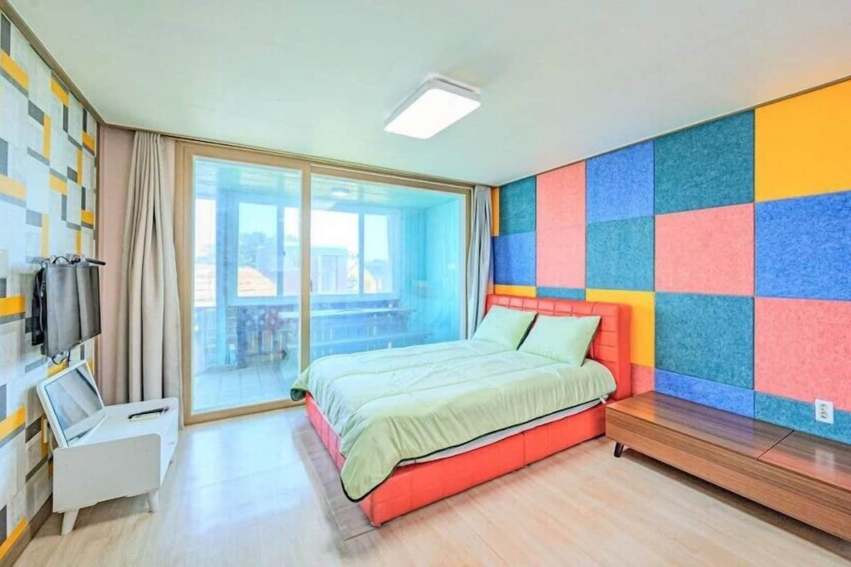 A modern bedroom with a bed, a desk, and a colorful wall.