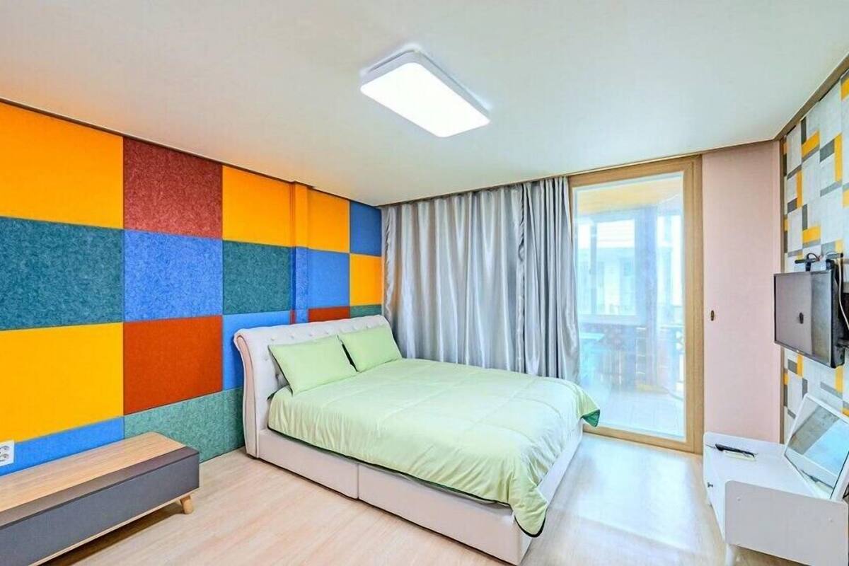 A modern bedroom with a colorful wall, a bed, a desk, and a TV.
