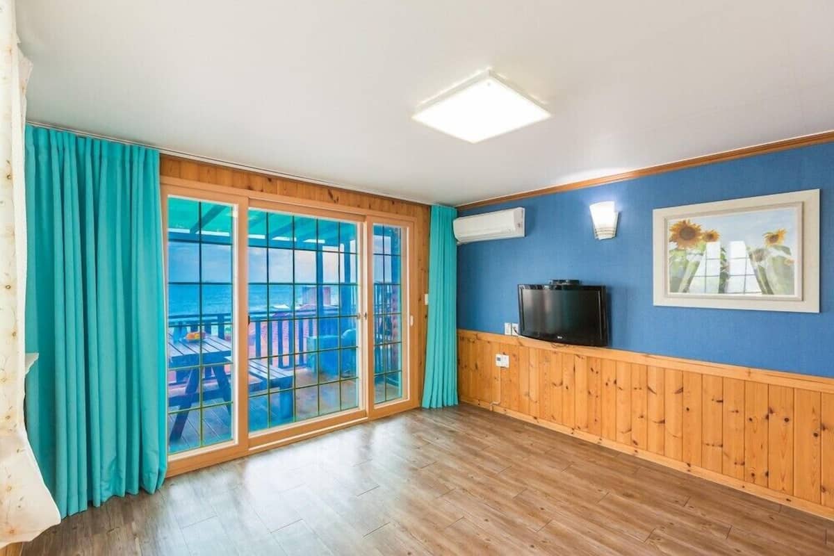 A room with wooden flooring, a sliding glass door leading to an outdoor deck, a mounted TV, and a framed picture on the wall.