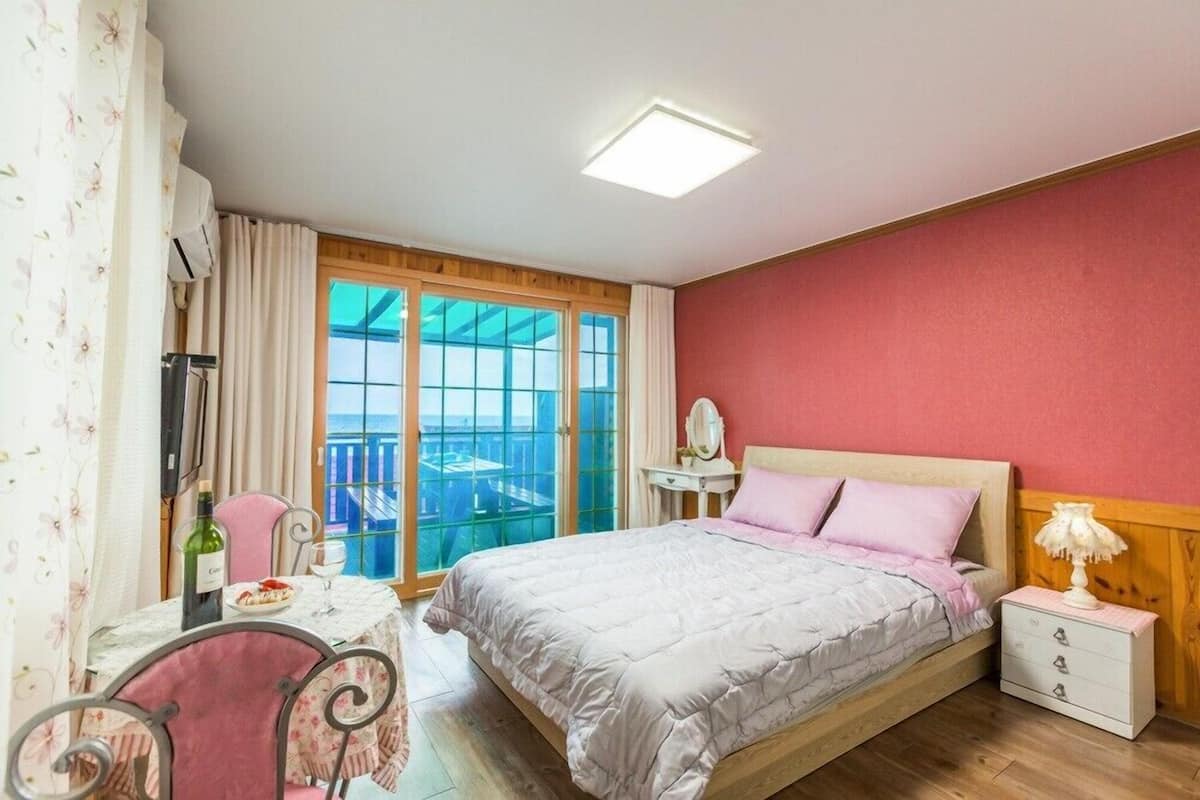 A bedroom with a bed, bedside table, and a view of the sea through large windows.