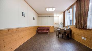 Una habitación con piso de madera, un sofá de cuero marrón, una mesa de comedor con sillas y una ventana con cortinas.
