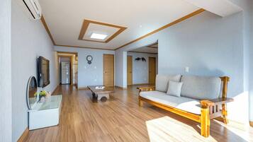 A spacious living room with wooden flooring, a sofa, a coffee table, and a TV on a stand.