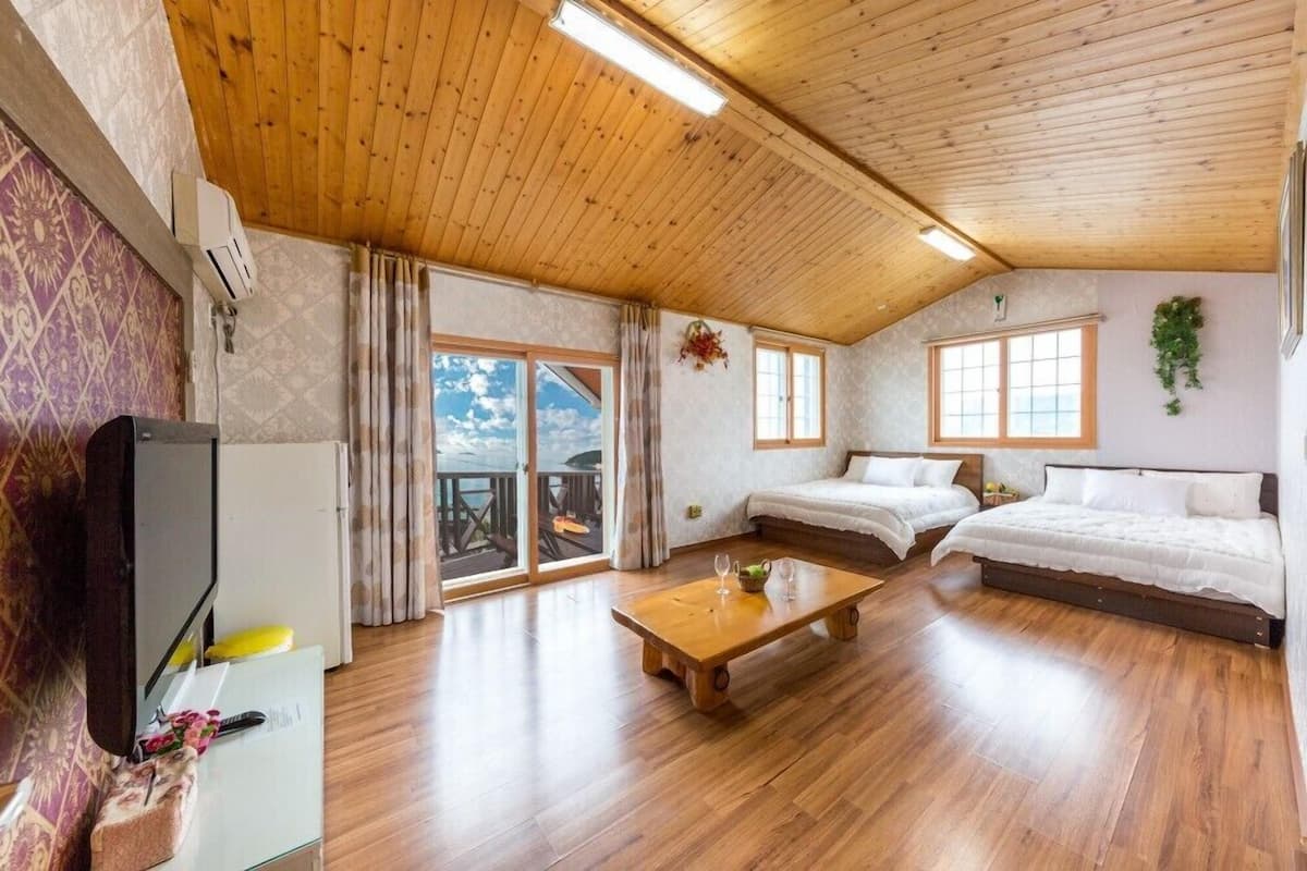 Una habitación con paneles de madera, una cama, un sofá, una mesa de centro y un televisor.