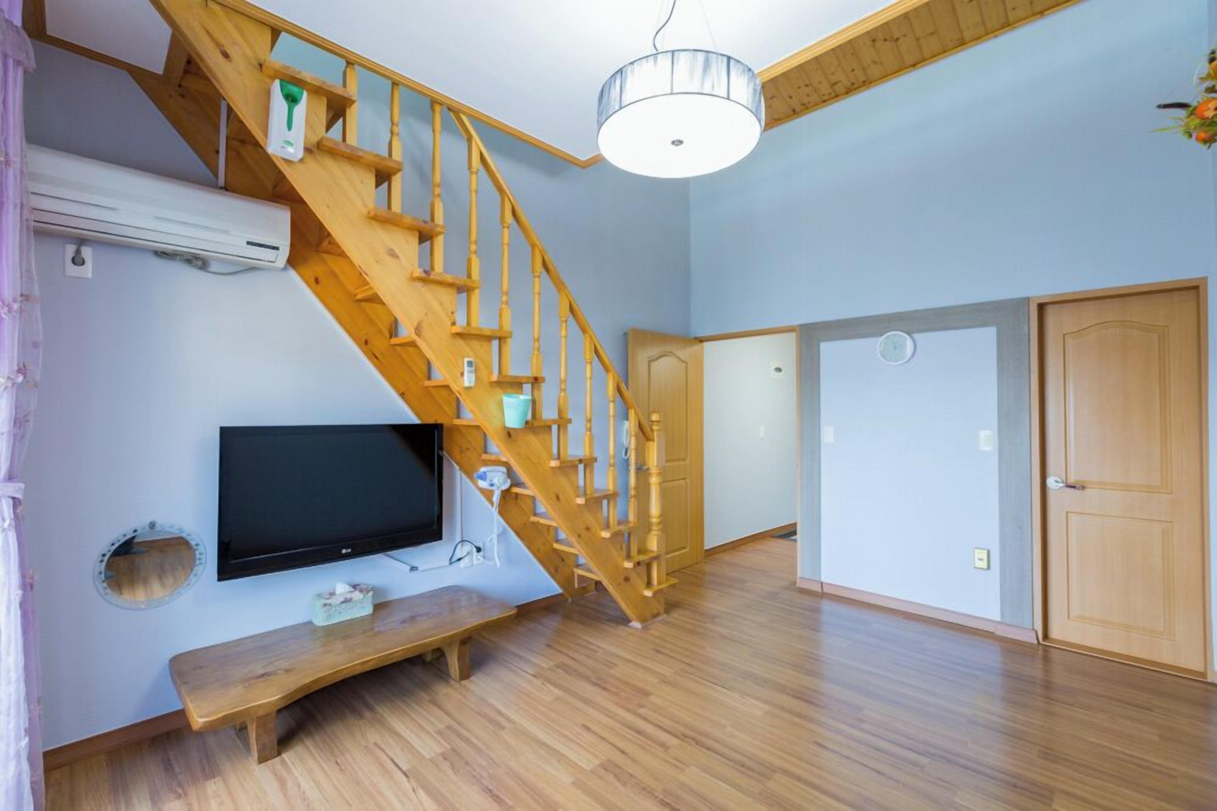 A room with a wooden staircase, a flat-screen TV, a bench, and a ceiling light fixture.