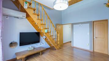 A room with a wooden staircase, a flat-screen TV, a bench, and a ceiling light fixture.