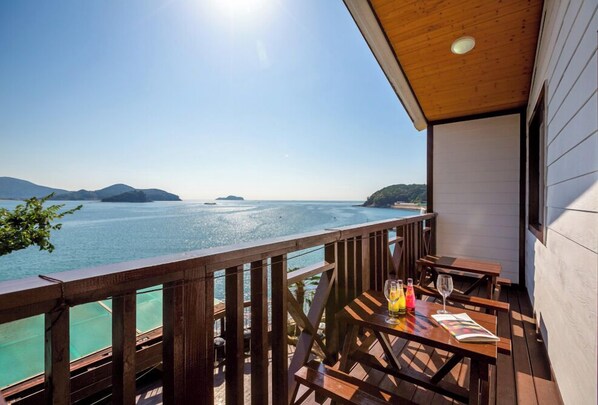 A wooden deck with a table and chairs overlooking a calm sea and distant islands.
