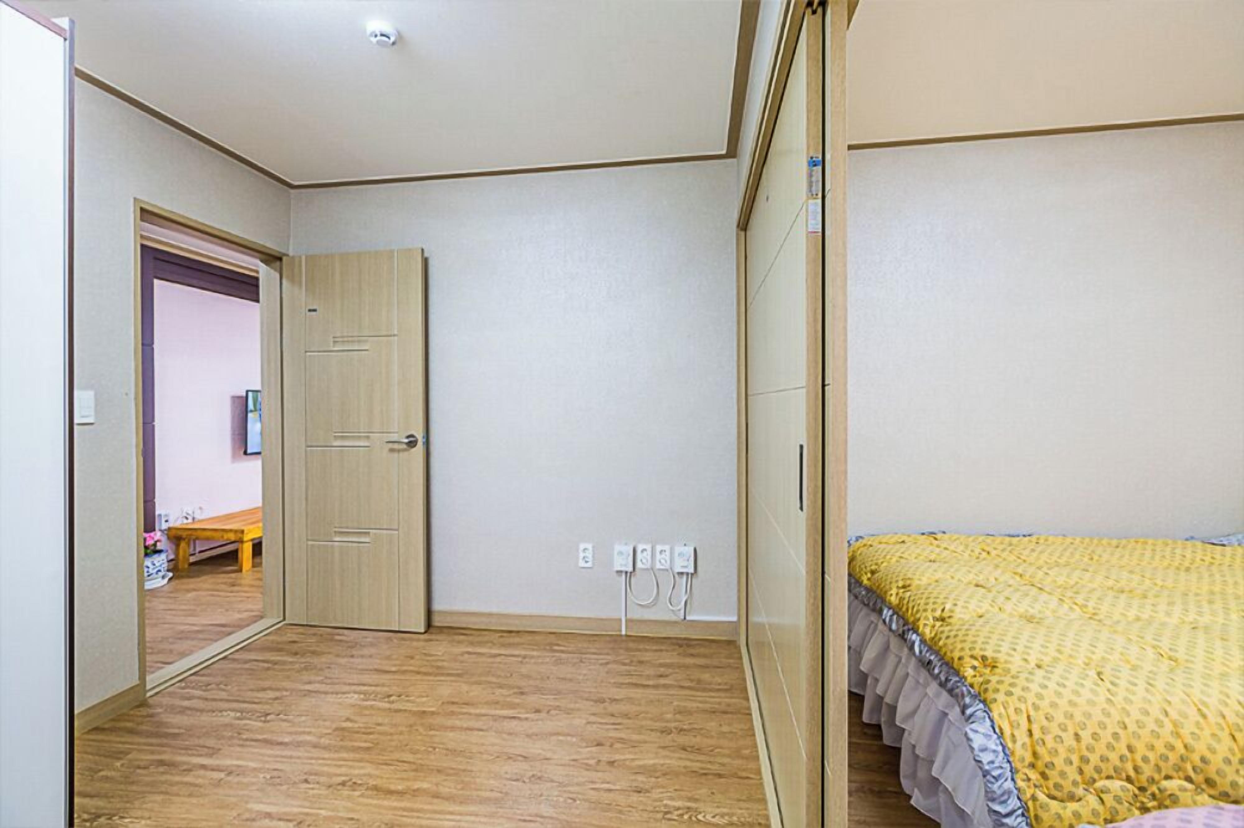 A bedroom with a wooden floor, a bed with a yellow bedspread, a wardrobe, and a door leading to another room.
