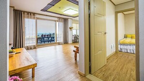 Una habitación amplia con piso de madera, un balcón con vistas, una zona de comedor con mesa y sillas, y una cama con cabecera amarilla.