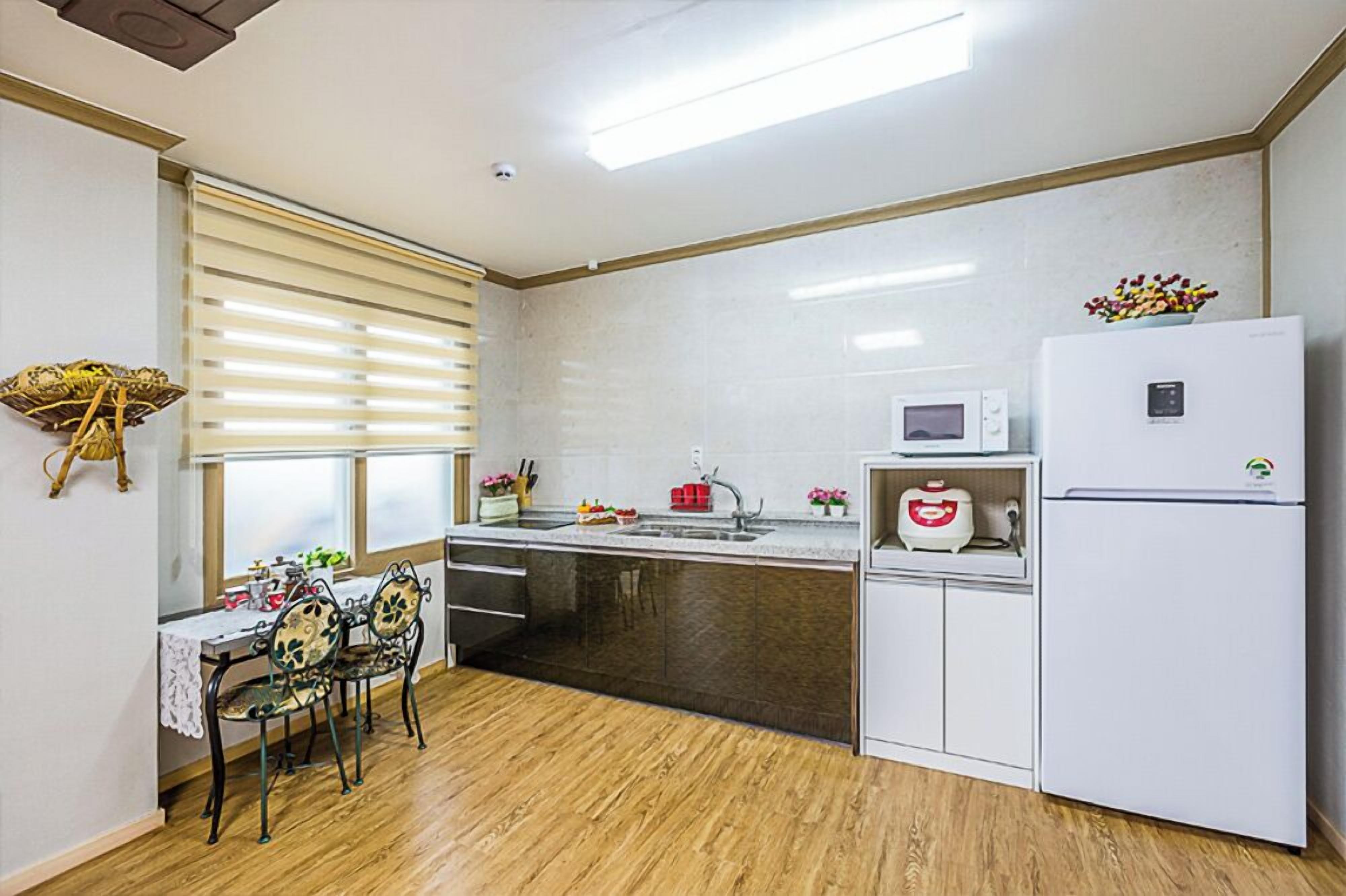 A compact kitchen with a wooden dining table, white cabinets, a refrigerator, and a microwave.