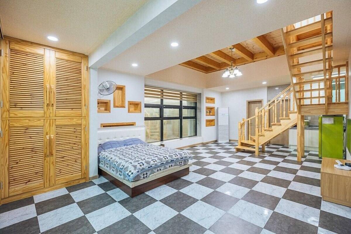 Ein Schlafzimmer mit Schachbrettfußboden, einem Holzschrank, einem Bett, einem Fenster und einer Holztreppe.