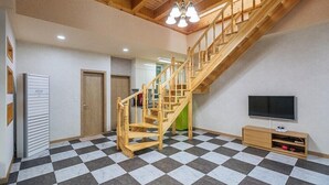 A spacious room with a checkered floor, a wooden staircase, a television, and a small cabinet. - Sun and moon pension (Ansan)