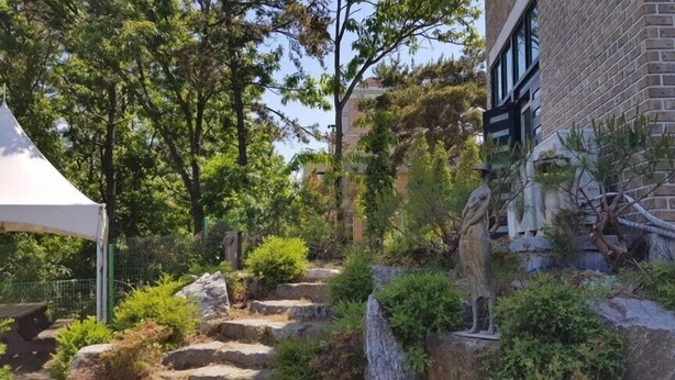 A courtyard with a statue, a tent, and a brick building. - Sun and moon pension (Ansan)