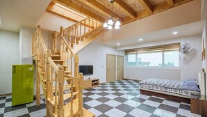 A spacious room with a checkered floor, a wooden staircase, a bed, a television, and a window with blinds. - Sun and moon pension (Ansan)