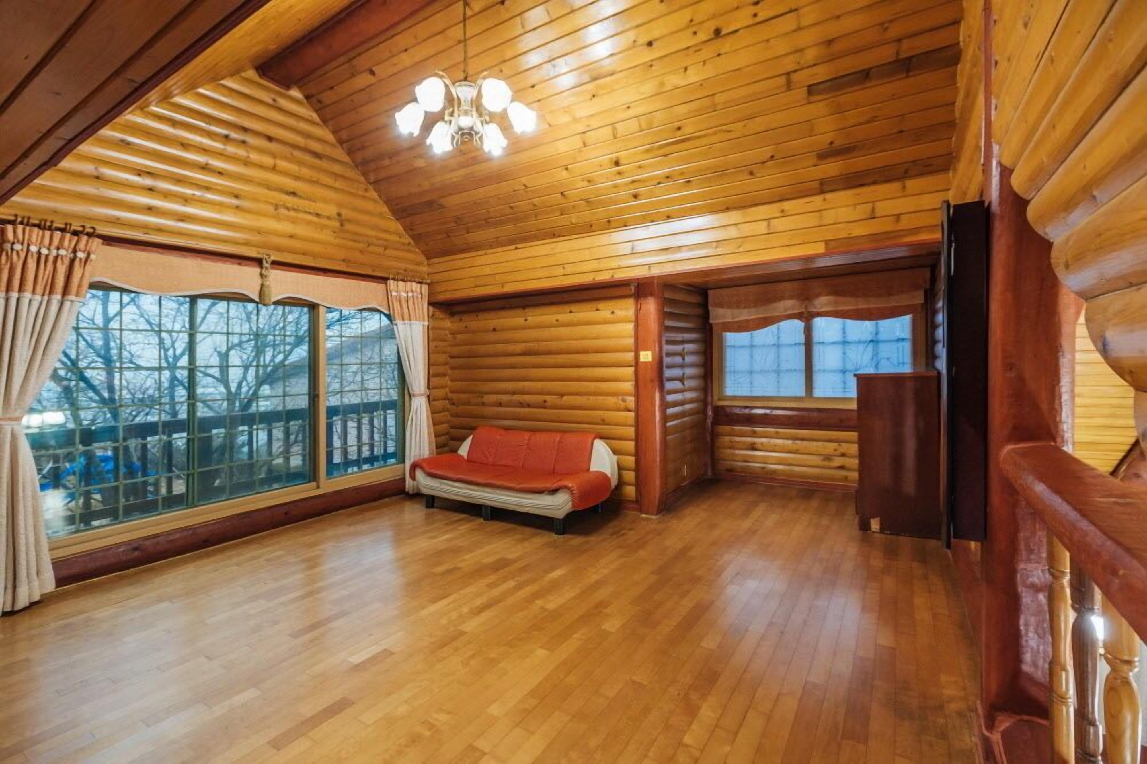 Interno di una baita in legno con pareti e soffitto in legno, un divano e ampie finestre.