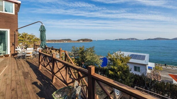 Une terrasse en bois, agréée de mobilier d’extérieur, qui offre une vue sur une étendue d’eau et sur des îles lointaines.