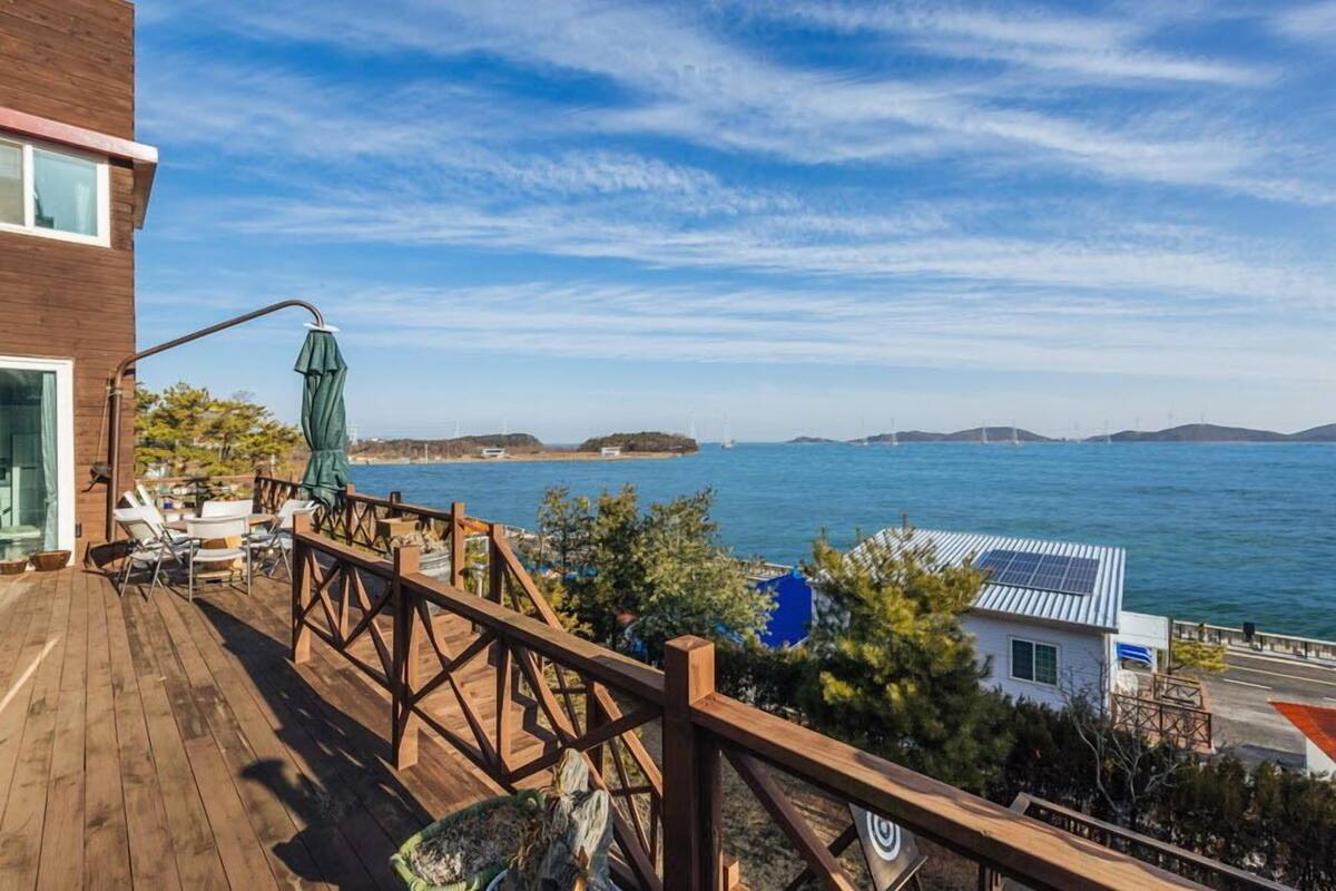 Una terraza de madera con mobiliario exterior, vista a un cuerpo de agua y unas islas distantes.