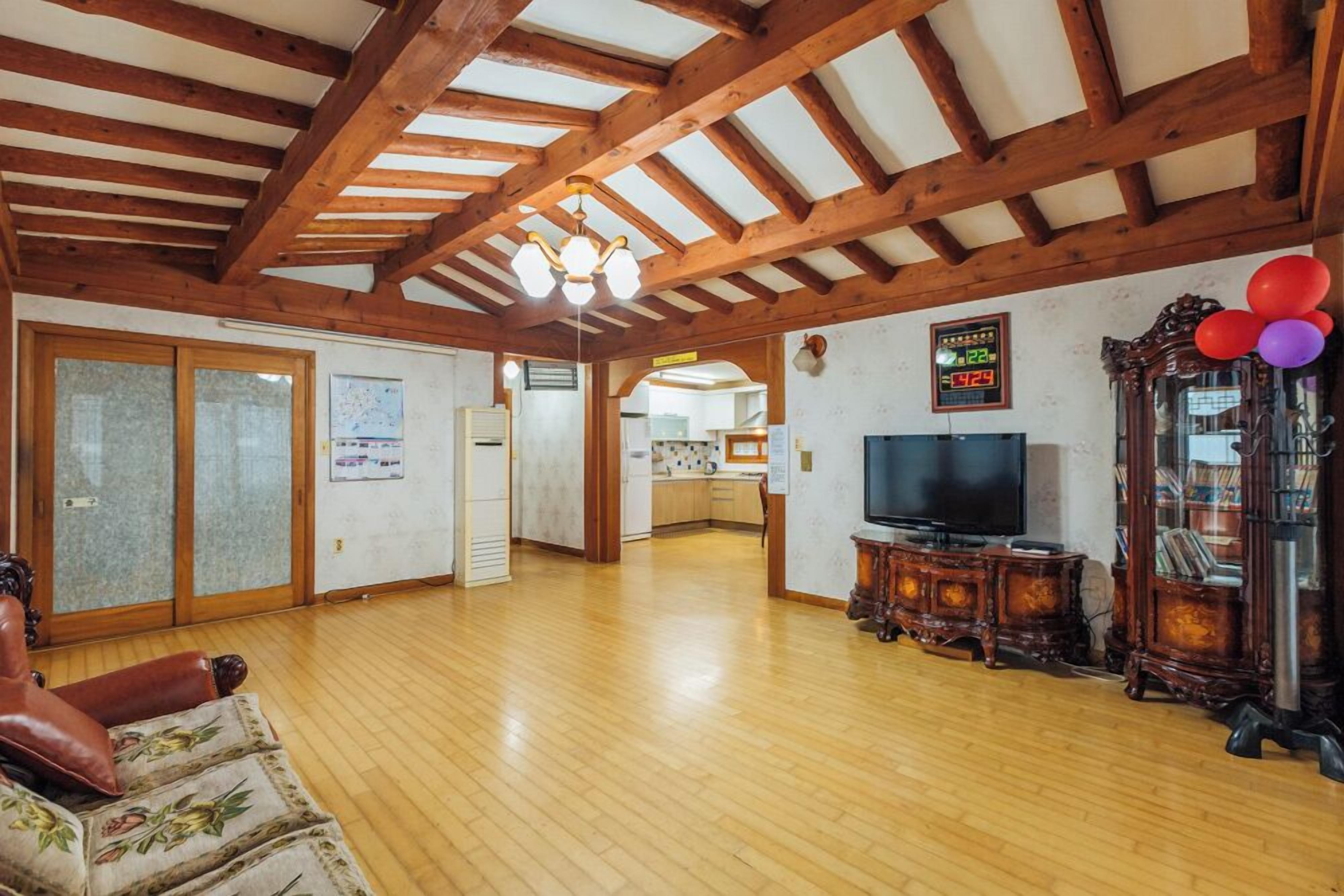 Un salón amplio con vigas de madera, televisor, armario y una ventana grande.