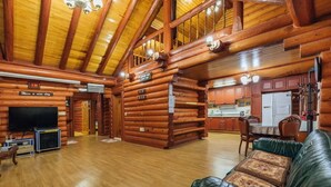 L’intérieur d’une cabane en rondins, avec un plancher en bois, un canapé en cuir, un téléviseur et un coin cuisine.