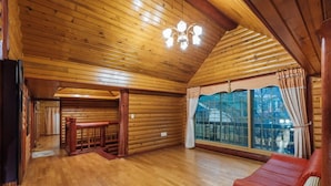 L’intérieur d’une cabane en rondins, avec un plancher en bois, un banc rembourré de couleur rouge, un coin repas et de grandes fenêtres dotées de rideaux.