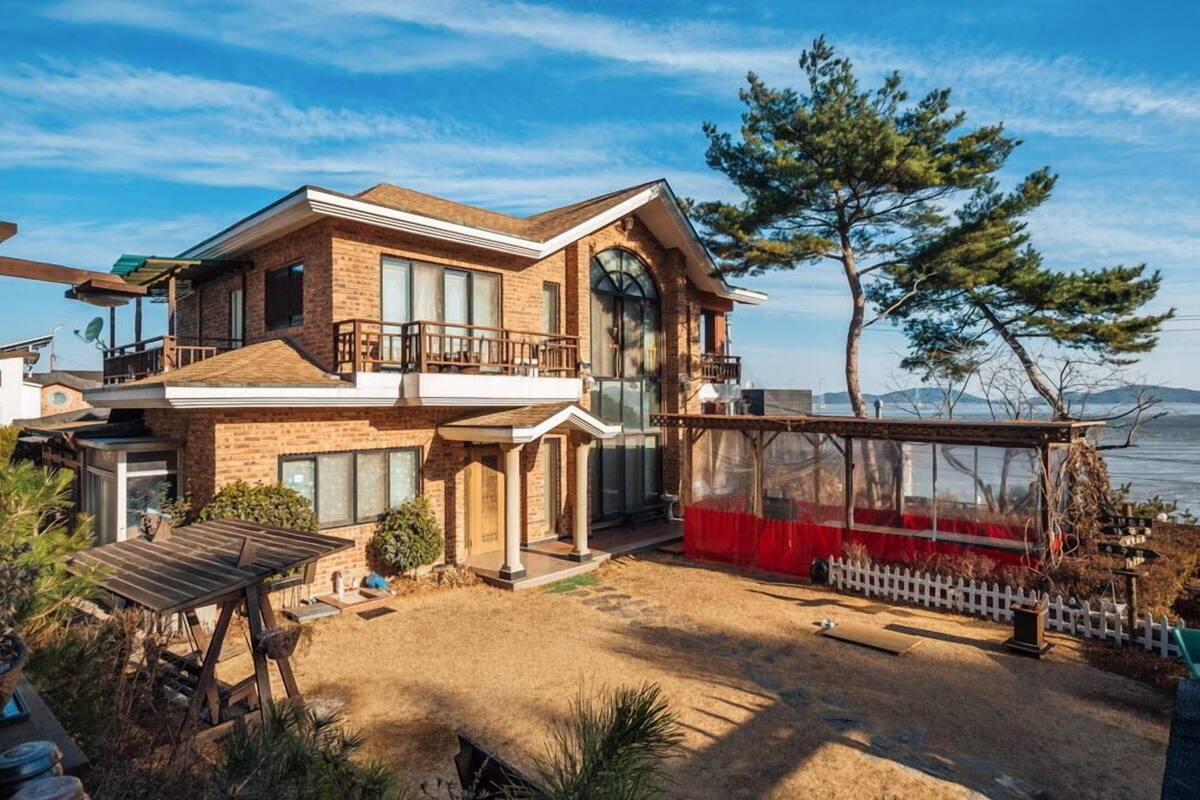 Una casa de dos pisos con balcón, un patio cubierto y vista al agua.