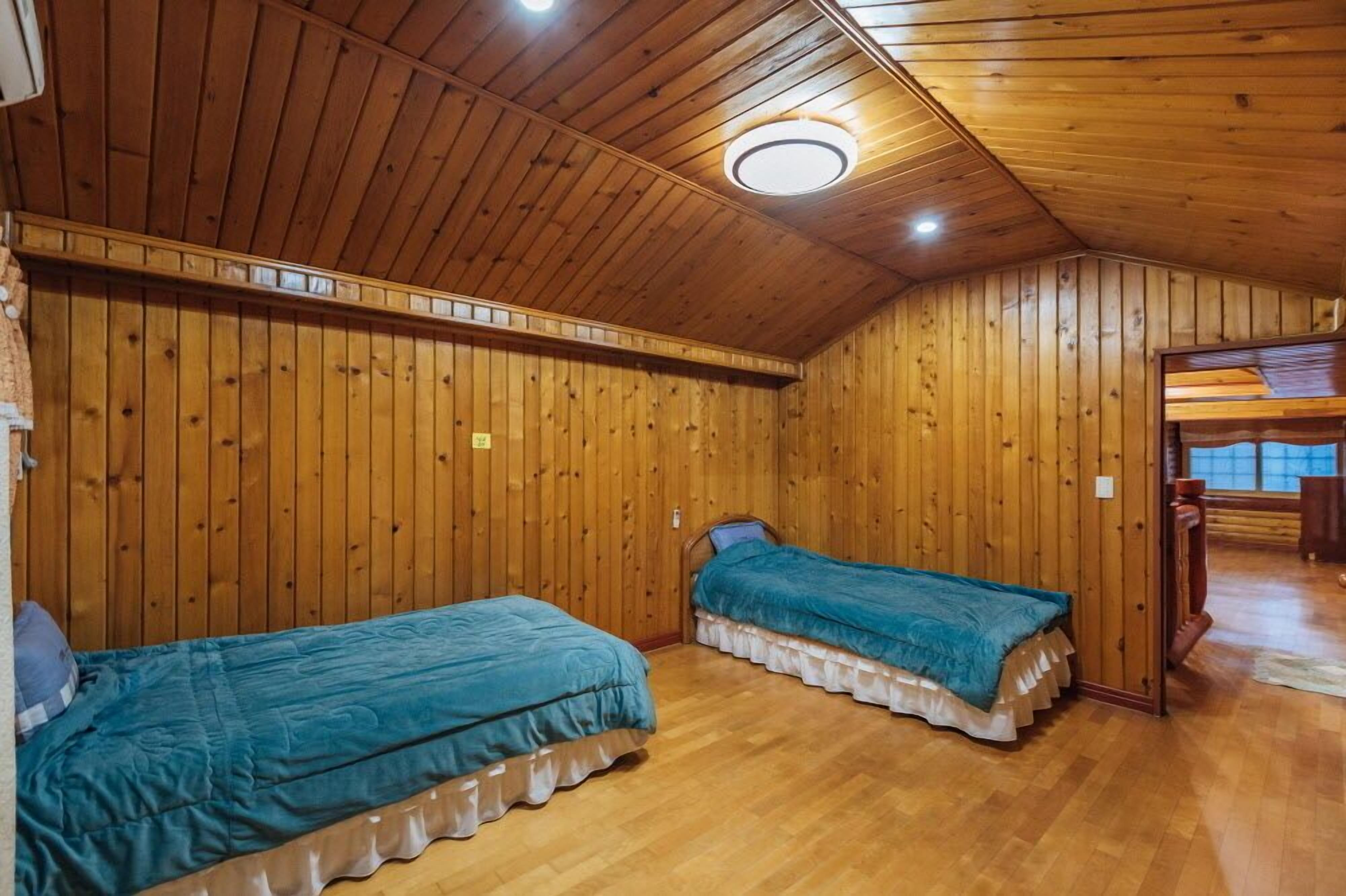 Een kamer met houten wanden en plafond, twee eenpersoonsbedden met blauwgroene beddengoed, en een houten vloer.