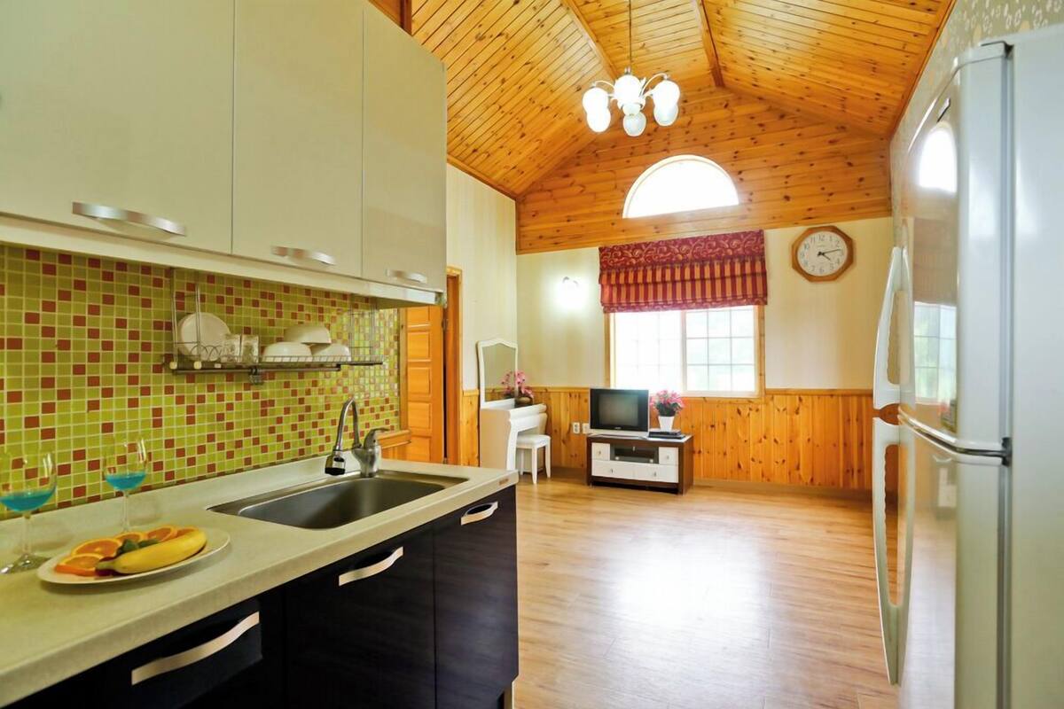 Une cuisine avec un plafond en bois, un évier et un coin repas équipé d’une télévision.