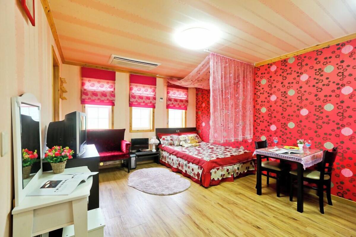 Une chambre à coucher avec un lit, un bureau, une chaise, un miroir et une fenêtre avec des rideaux.