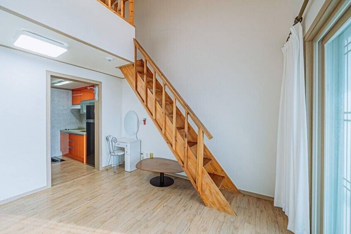 A spacious room with a wooden staircase, a dining area, and a kitchen visible through an open door.
