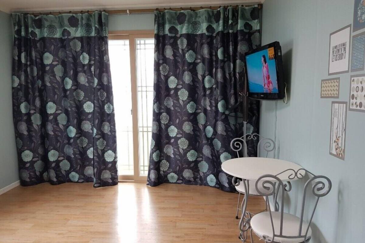 A room with a wooden floor, a white table with a metal chair, and a TV on the wall.